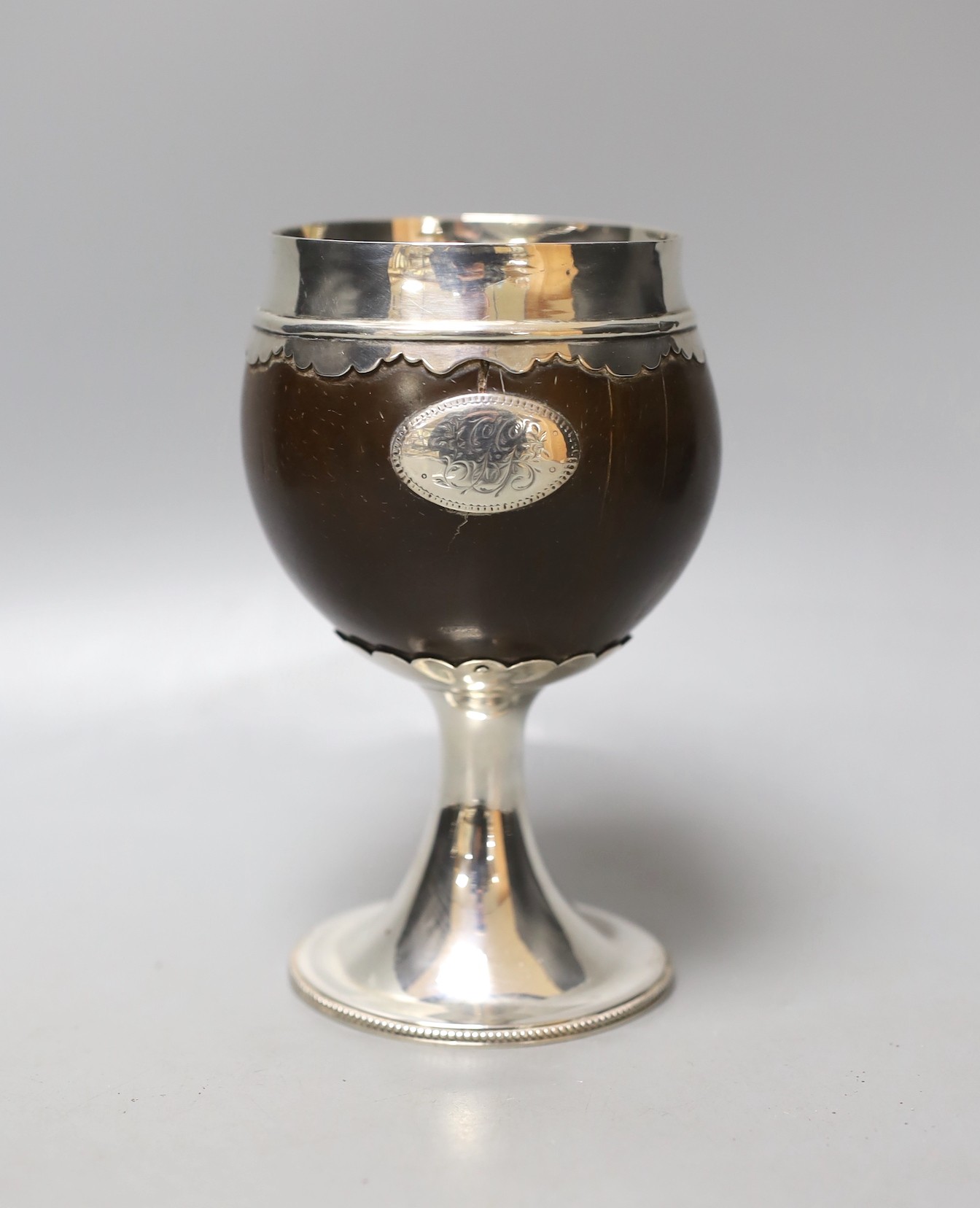 An early 19th century white metal mounted coconut cup, on pedestal stem, unmarked, height 15.6cm, gross weight 290 grams.